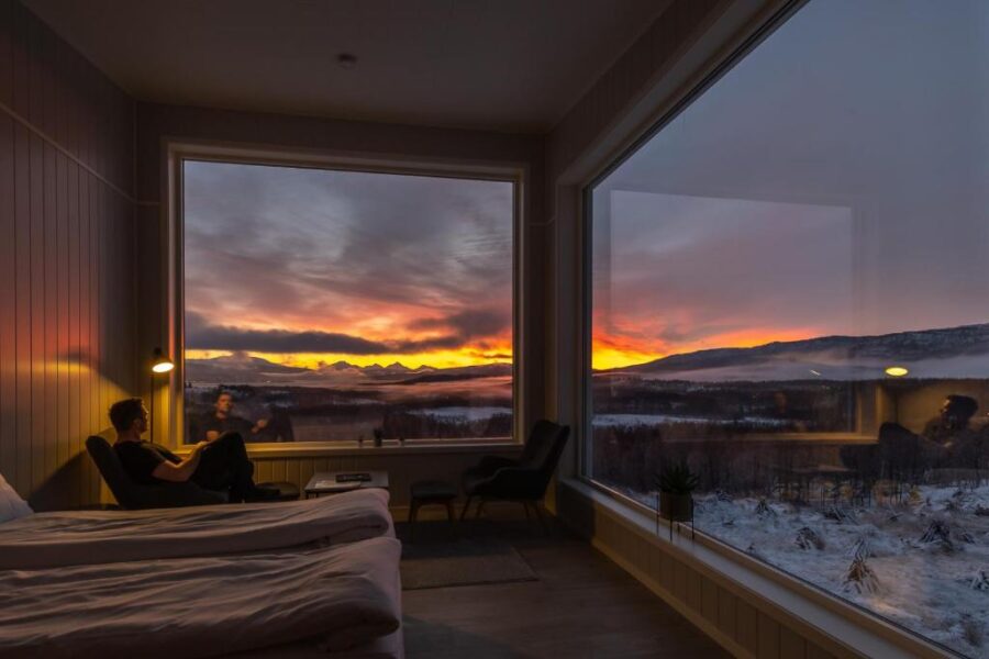 In a bedroom with mountain views, a couple enjoys a serene moment together at the Aurora Borealis Observatory, Norway.