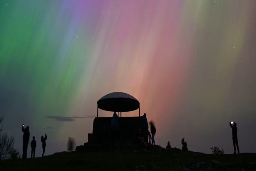 Aurora borealis illuminates night sky with silhouetted figures and observatory beneath vibrant colors.
