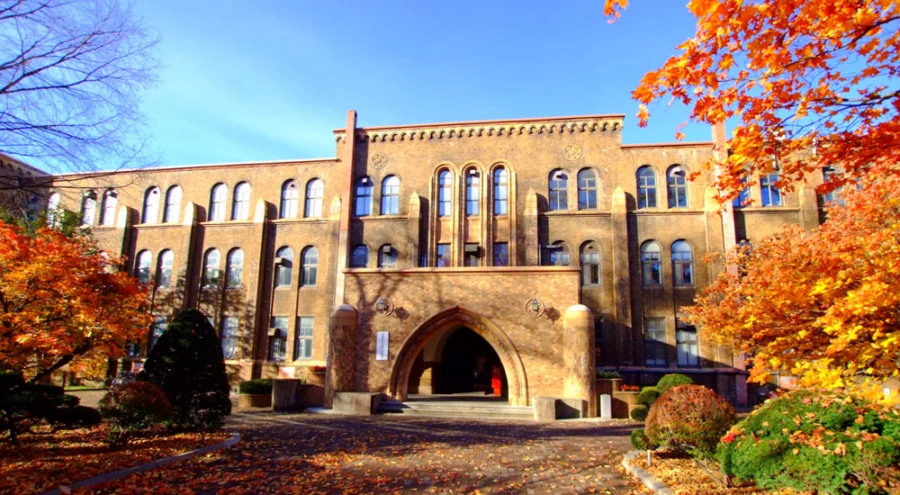 Hokkaido University brick campus building with arched entrance and colorful autumn trees under blue sky.