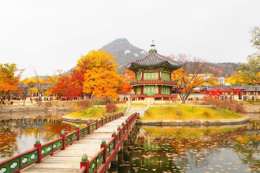 Autumn pavilion surrounded by vibrant foliage and tranquil waters at Gyeongbokgung Palace.