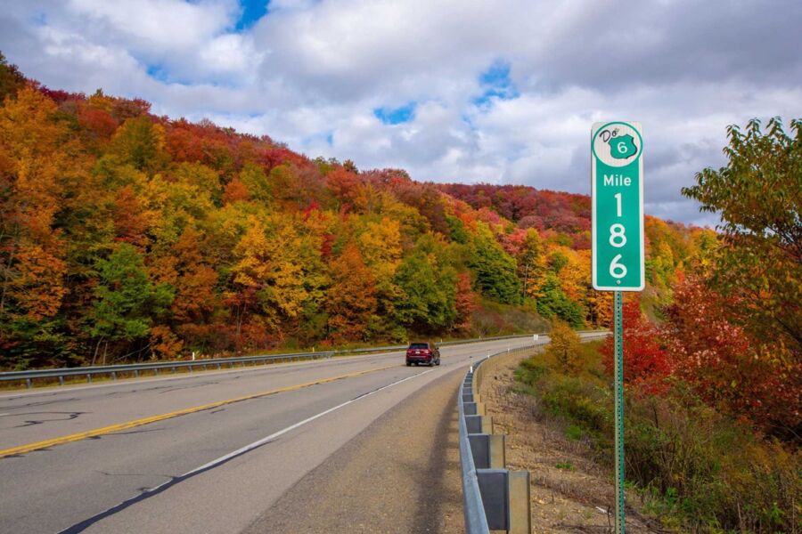 Scenic Route 6 Mile 186: Autumn foliage, clear sky, vibrant colors, red car, serene drive.