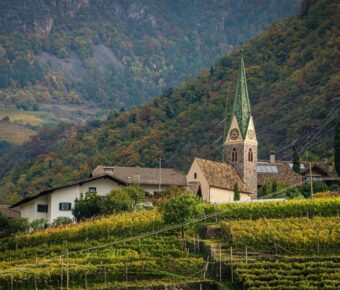 Picturesque village with church, vineyards, rustic homes, mountainous backdrop, autumn colors.