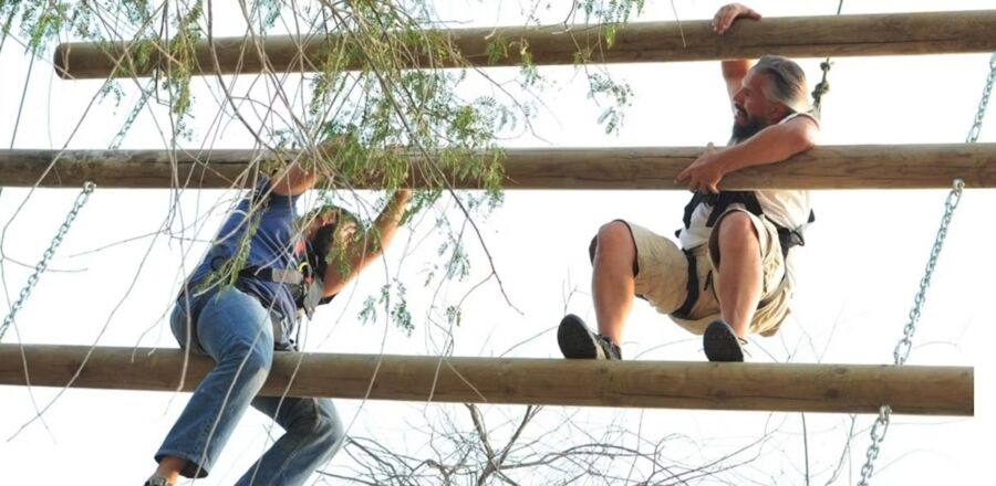 Two individuals navigate ropes in an obstacle course at Aventura Parks' Jacob’s Ladder Experience.

