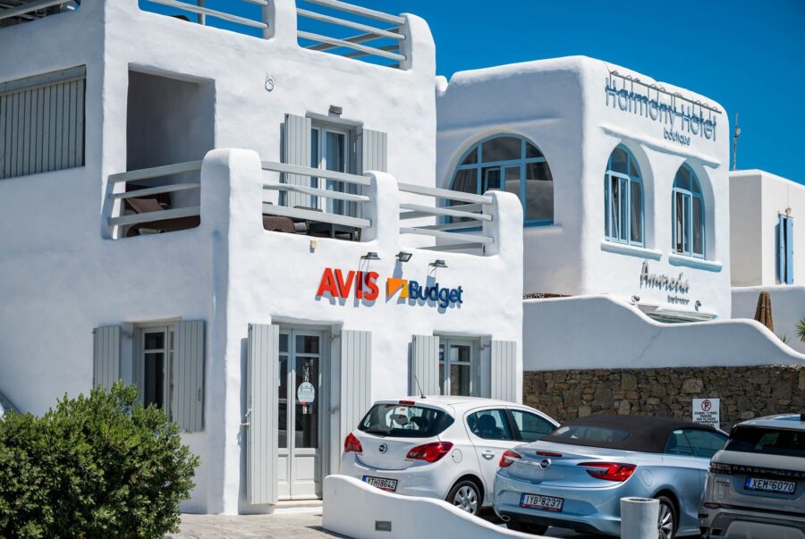 Car rental in Greek island setting with modern architecture and diverse vehicles.