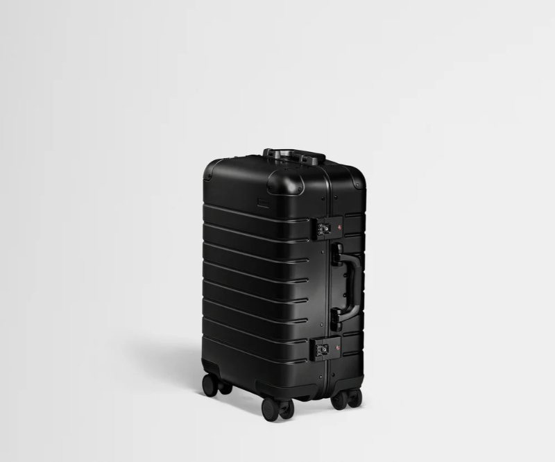 Side view of a black Away Aluminum carry-on suitcase with wheels, highlighting its modern design and secure locking feature.