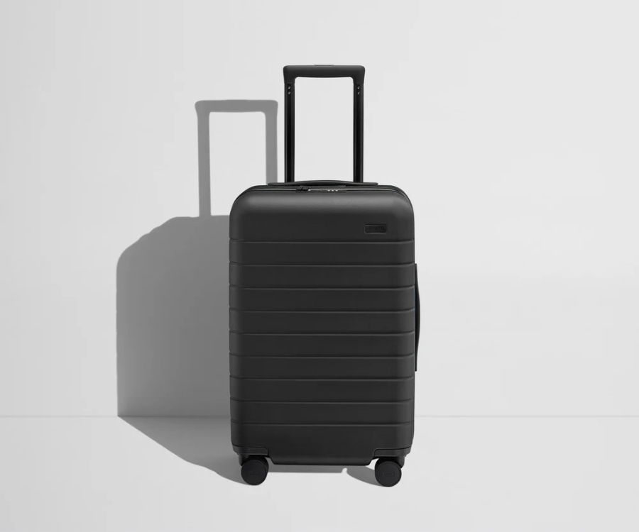 Black Away Carry-On Flex suitcase with wheels resting on a white surface.