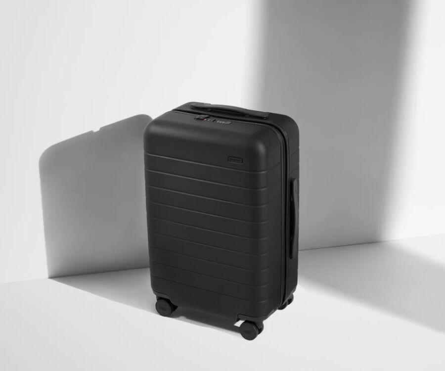 Jet black Away Carry-On suitcase with wheels, featuring a shadow on the surface beneath it.
