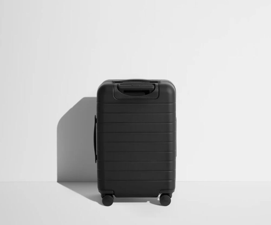 Away carry-on luggage: a black suitcase with wheels placed on a clean white surface.

