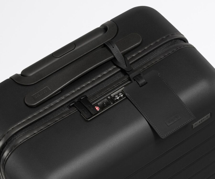 Close-up image of a black Away carry-on suitcase with an attached luggage tag.

