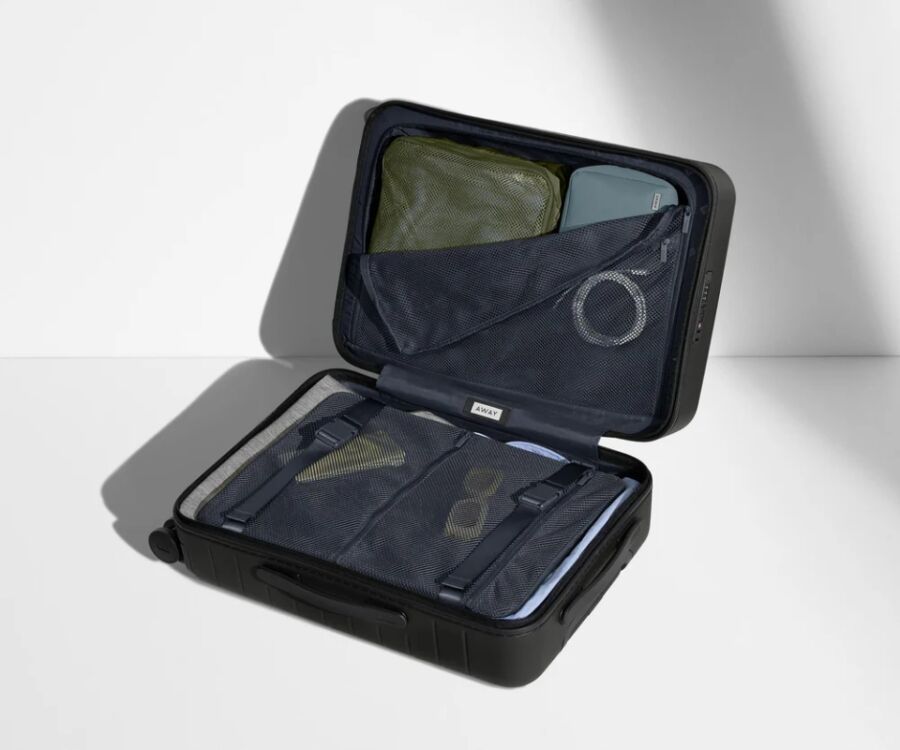Black carry-on suitcase featuring a green and blue zipper, identified as Away brand luggage, displayed on a flat surface.
