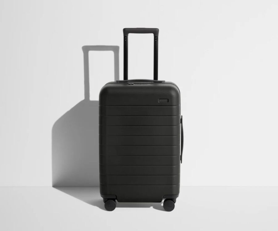 Black Away carry-on suitcase with wheels resting on a white surface