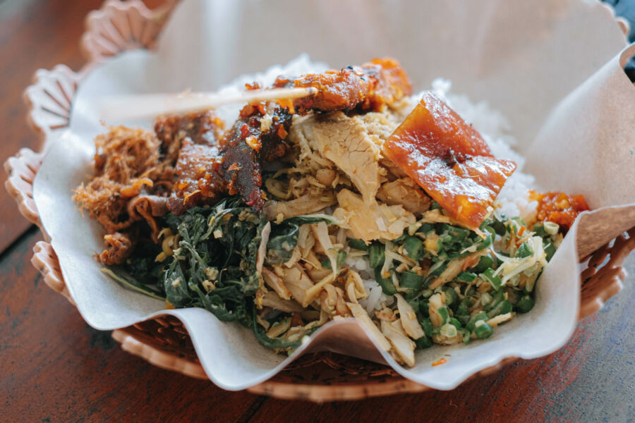 Close-up of a plate featuring Balinese nasi babi guling, showcasing roasted pork, rice, and traditional garnishes