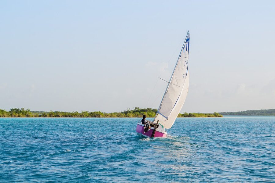 Sailboat with a small white sail glides across the tranquil waters of Bacalar Lagoon.