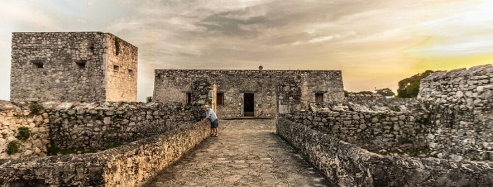 The ruins of an old castle silhouetted against a vibrant sunset in Bacalar, Quintana Roo, Mexico.