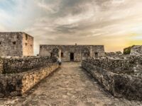 The ruins of an old castle silhouetted against a vibrant sunset in Bacalar, Quintana Roo, Mexico.