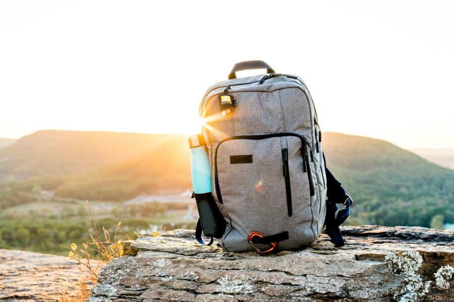 Gray hiking backpack on a rock with water bottle at sunrise outdoors.