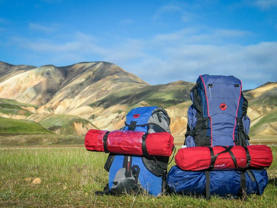Blue hiking backpacks on a meadow facing rolling hills and clear mountain sky.