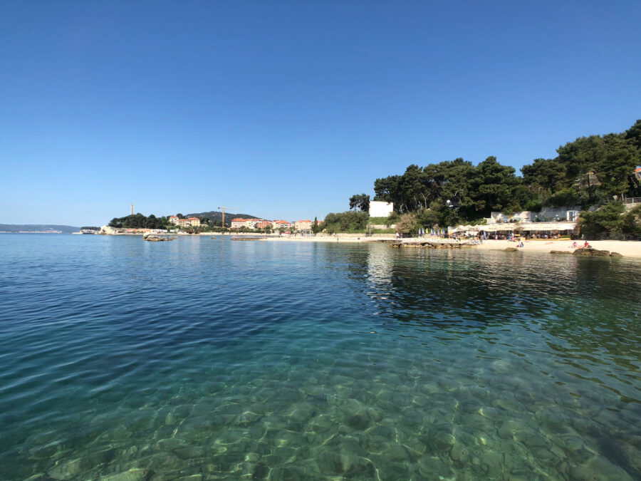 Bacvice Beach in Split, Croatia, features golden sand, clear blue water, and sunbathers enjoying a warm, sunny day.