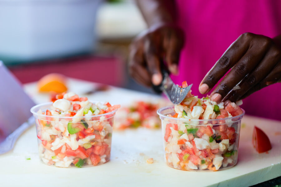 Man prepares Bahamian conch salad, finely chopping conch and colorful vegetables on a cutting board