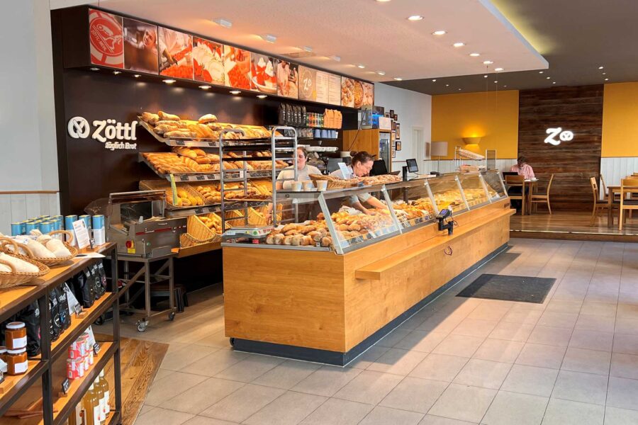 Bakery cafe counter with glass display of breads, pastries, coffee station, and seating.