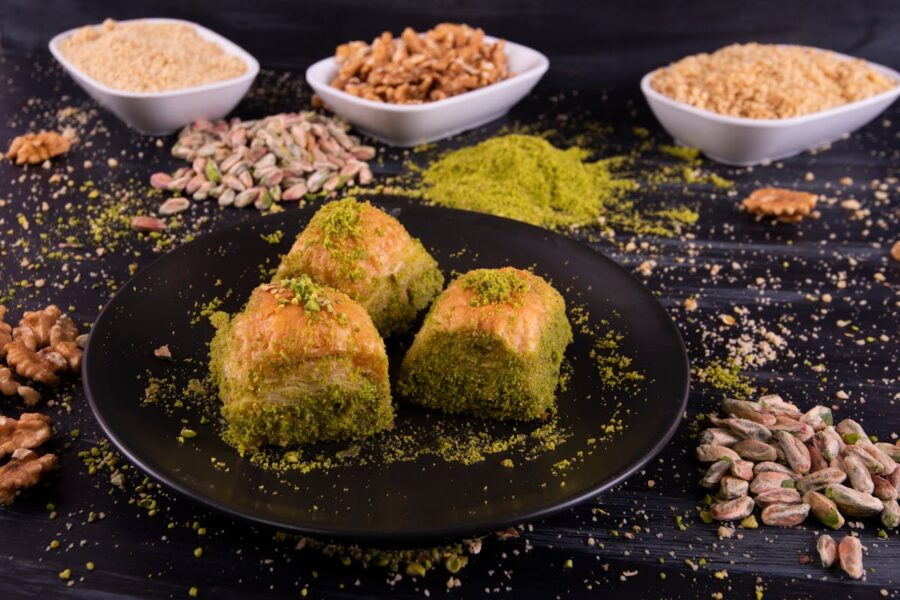 Plate of golden-brown triangular baklava with pistachios, surrounded by assorted nuts.
