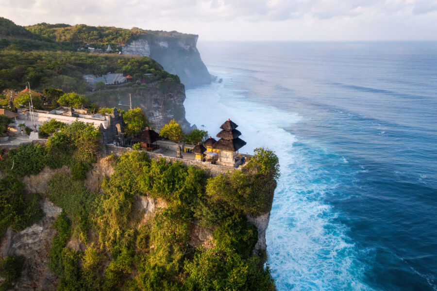 Aerial view of Uluwatu Temple in Bali, Indonesia, bathed in the warm light of sunrise, overlooking the ocean