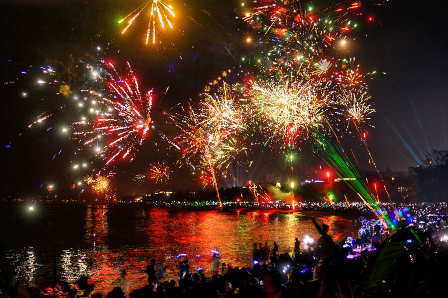 Colorful fireworks illuminate the night sky over a lively New Year's Eve celebration in Bali, with people enjoying the festivities