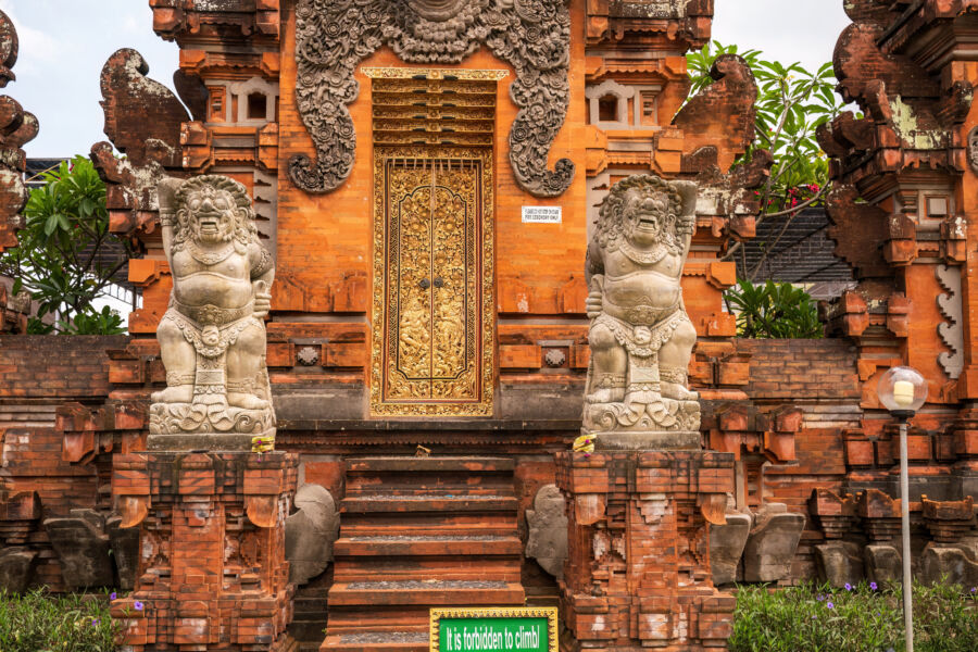 Guardian figures stand at a Balinese temple gate, showcasing intricate carvings and a dazzling gold door, reflecting local artistry