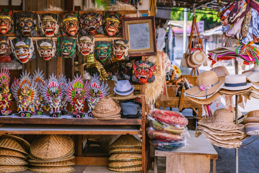 Shelves in a Balinese souvenir shop feature vibrant wooden masks, statues, and straw hats in Bali, Indonesia
