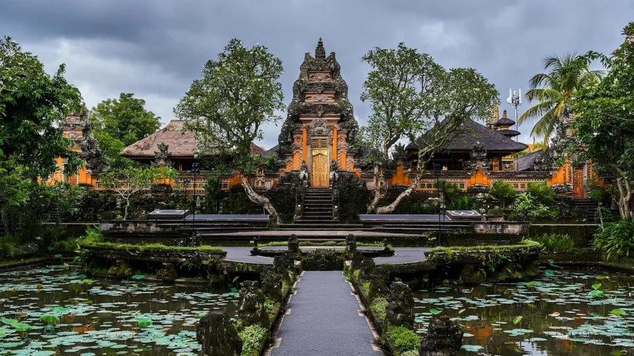 Balinese temple in Ubud with stone path, lotus ponds, tropical greenery and dramatic stormy sky.