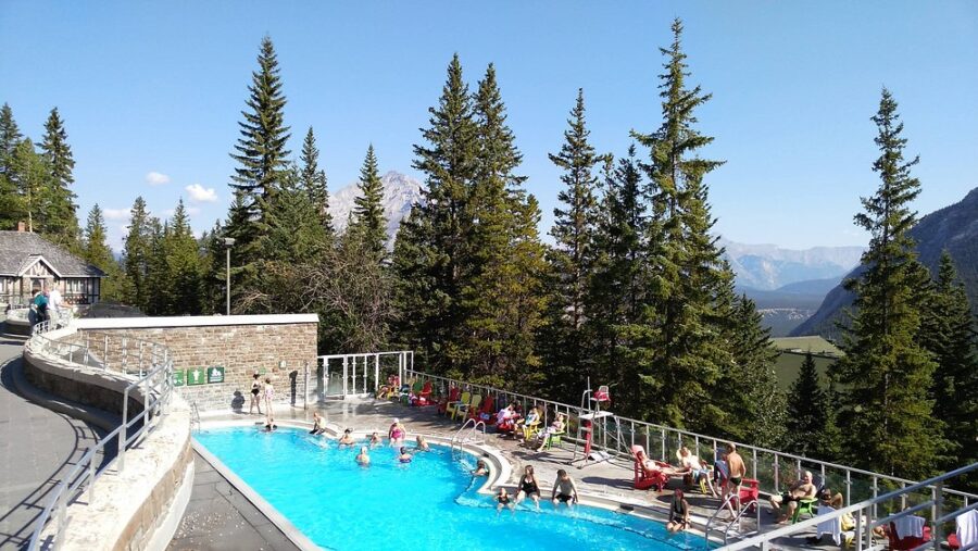 People swim in a pool at Banff Upper Hot Springs, with mountains visible in the background.
