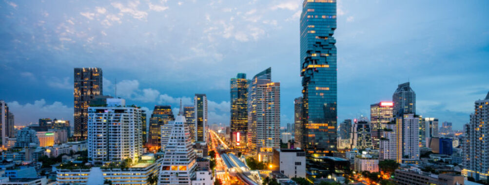Aerial view of Bangkok's skyline at night, featuring skyscrapers and the BTS skytrain weaving through the downtown area