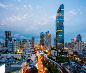 Aerial view of Bangkok's skyline at night, featuring skyscrapers and the BTS skytrain weaving through the downtown area