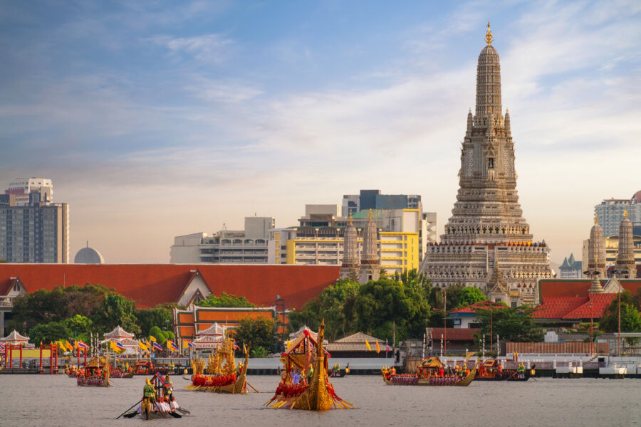 Traditional Thai royal boat on a river in Bangkok, with the iconic Wat Arun temple visible in the background