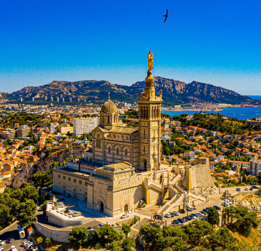 Aerial view of Marseilles iconic Notre-Dame de la Garde basilica, Mediterranean Sea, and cityscape.