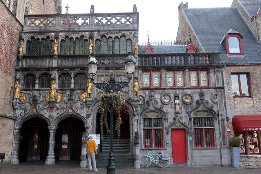 The Basilica of the Holy Blood in Bruges features intricate architecture, with a bicycle positioned at its entrance.
