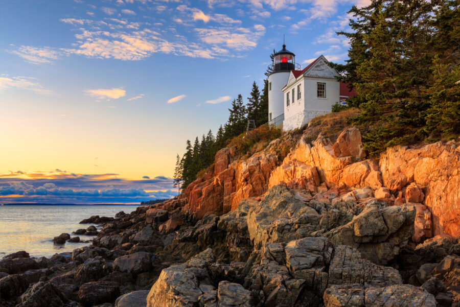 Bass Head Light stands tall on a rocky cliff, overlooking the ocean at Acadia National Park, surrounded by lush greenery.