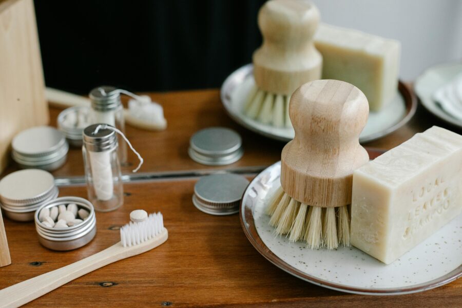 Eco-friendly personal care items with brush, soap, tins, and glass vials on wooden table.