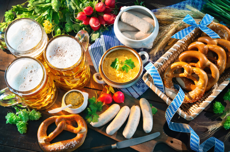 Bavarian sausages, pretzels, sweet mustard, and beer mugs on a rustic table.