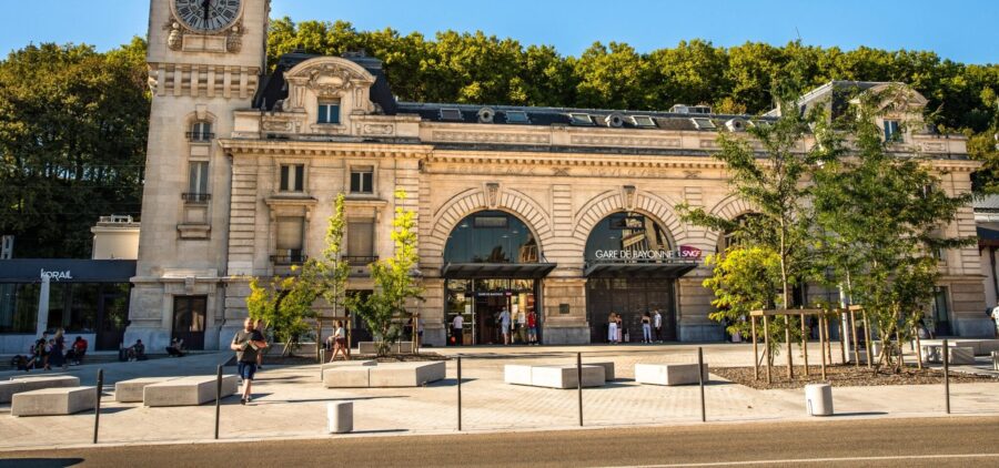 Bayonne train station facade with clock tower, SNCF entrance, plaza, and surrounding trees.