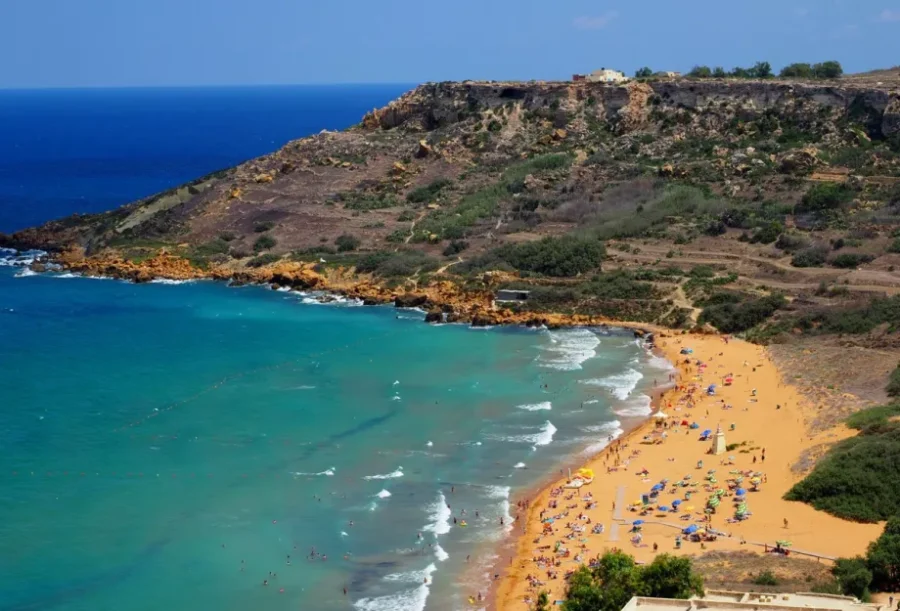 Aerial view of Ramla Bay, Malta: golden beach and turquoise water with sunbathers.