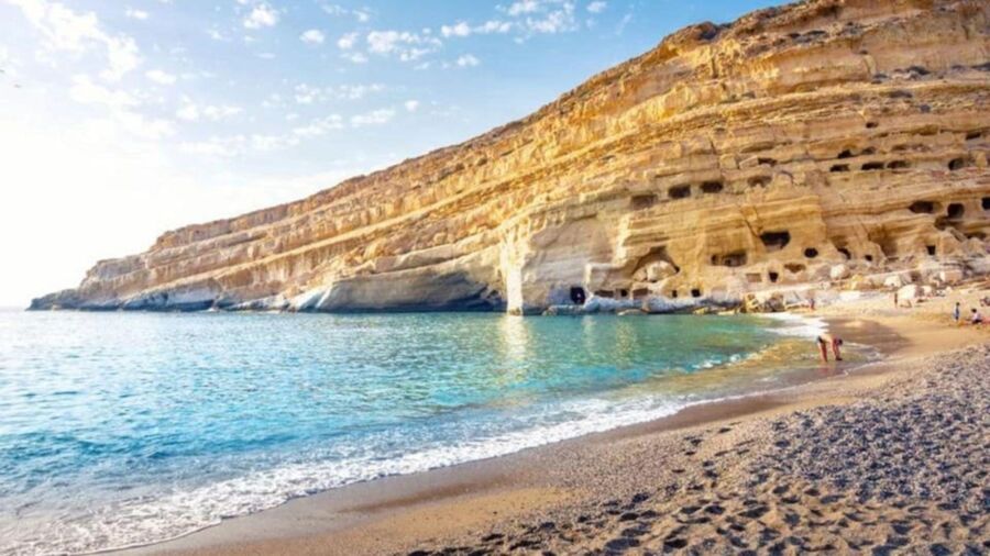 Serene beach with rocky cliffs, turquoise sea, sandy shore, and people enjoying the sun.