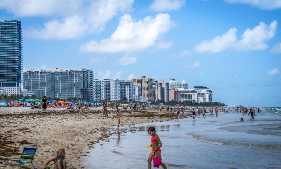 Lively Miami beach scene with families, skyscrapers, and ocean waves under a sunny sky.