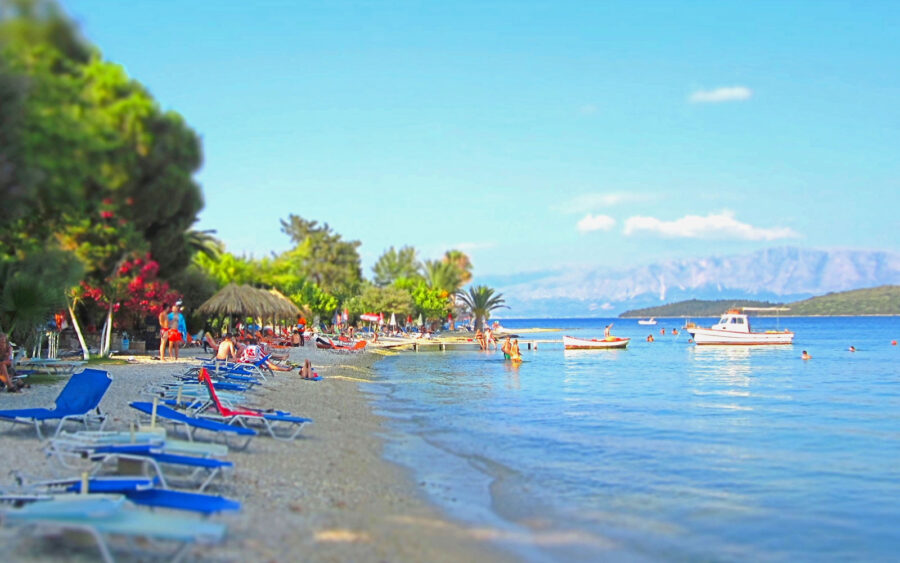 Tropical beach with lounge chairs, clear waters, boats, and scenic hills in the background.