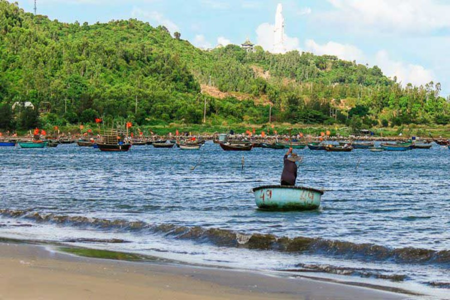 Man Thai Village fishing boats anchored in bay with round basket boat and green hillside backdrop.