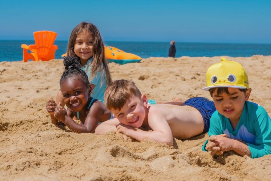 Children playing joyfully on a sunny beach with sand and ocean waves in the background.