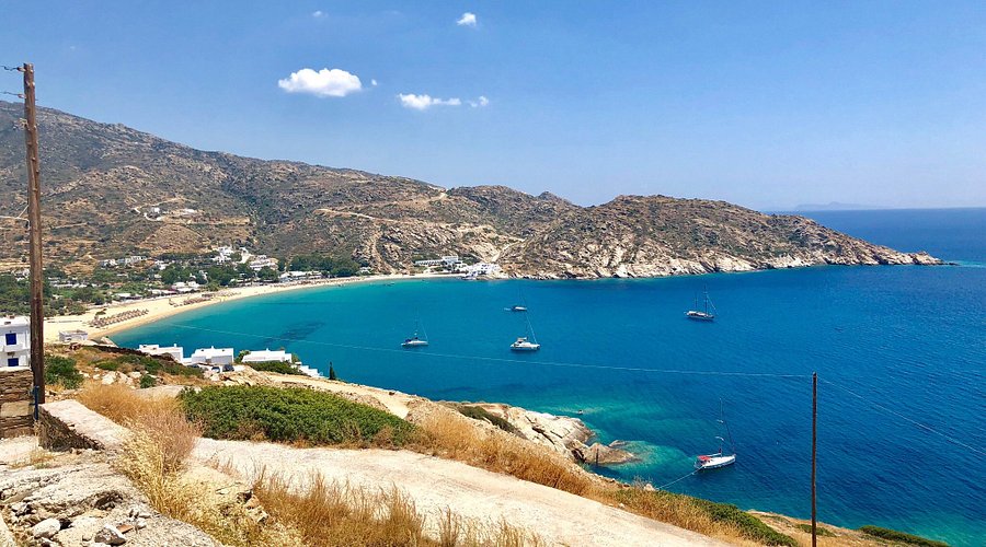 Azure Mylopotas Beach with boats, lush hills, and white buildings in serene Mediterranean setting.