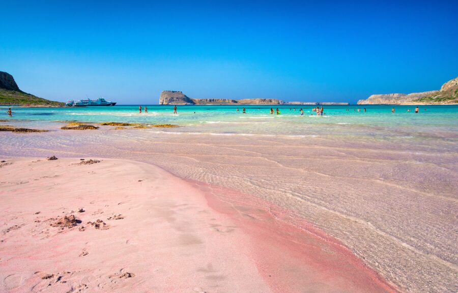 Stunning pink sand beach with turquoise water, clear skies, and vibrant summer activities.