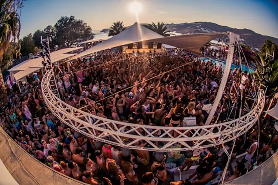 Sunset beach party with lively crowd, music, palm trees, and vibrant summer atmosphere.