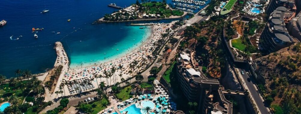 Aerial view of tropical Gran Canaria resort with beach, pools, marina, and vibrant atmosphere.